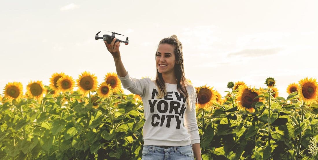 young woman holding a drone in a hand with sunflowers background and sunset golden light