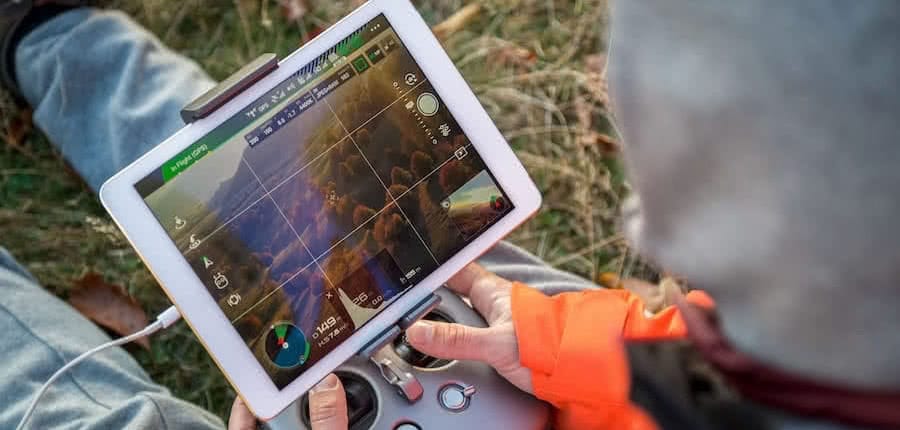 hands holding a rc controller with screen surveiying forest with drones