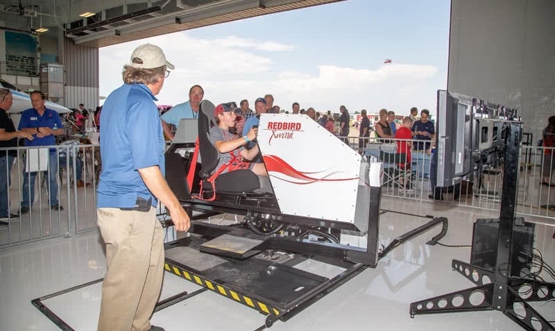 young man testing the full motion redbird xwind simulator in event with more people in the background
